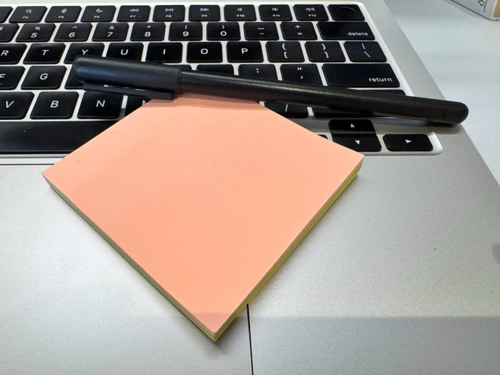 Blok papirića za beleške i olovka na tastaturi laptopa, spremni za listu pitanja pre izbora hostinga